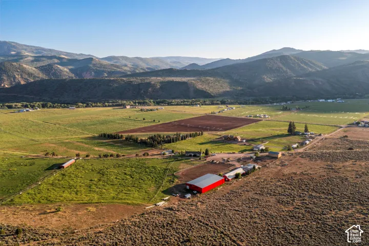 Expansive agricultural property featuring a red barn, multiple outbuildings, cultivated fields, and surrounding mountainous terrain
