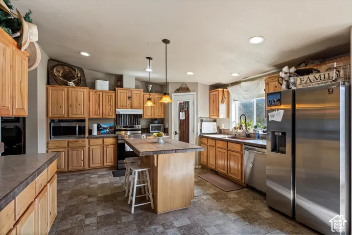 Spacious kitchen featuring warm wood cabinetry, a central island with bar seating, stainless steel appliances, and recessed lighting