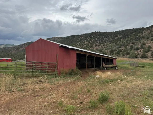 Red barn structure with an extended covered shelter and metal fencing, set against a mountainous backdrop