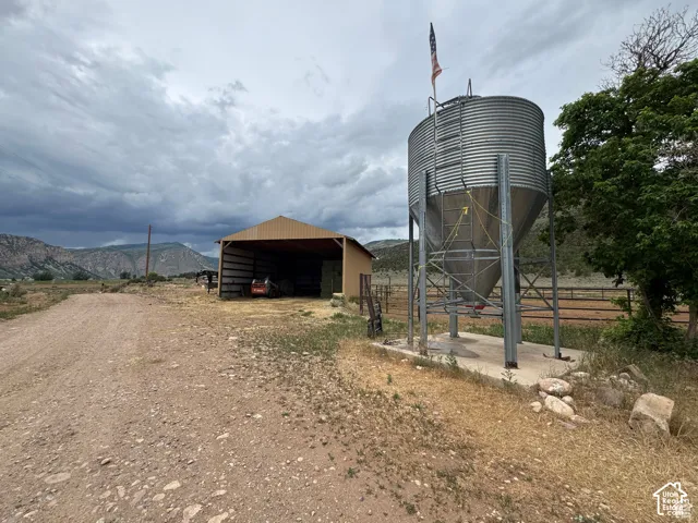 Corrugated metal silo on concrete foundation, open-sided barn structure, and a gravel drive
