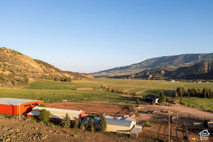 Expansive valley setting with mountainous terrain, multiple red agricultural buildings, a large dirt arena, and scattered green pastures