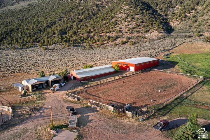 Large red metal building, open-air barn structure, fenced arena, additional outbuildings, and mountainous backdrop
