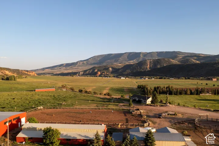 Expansive property with multiple barns, a large equestrian arena, and a single-story residence, all set against a backdrop of rolling hills and distant mountains