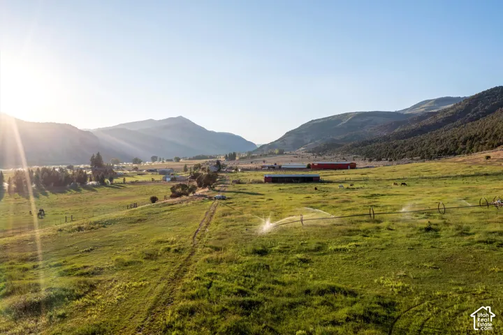 Expansive green pastures with irrigation system, surrounded by mountains and featuring multiple structures
