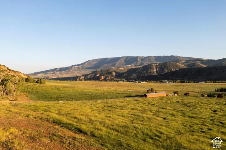 Expansive green fields with a single-story barn structure and distant mountainous terrain