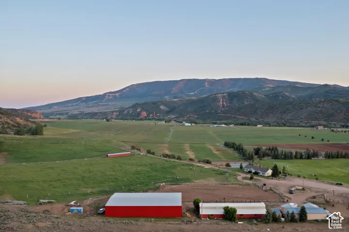 Expansive green fields with distant mountains, multiple red-roofed agricultural buildings, and a residential structure