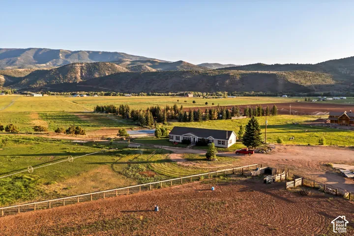Expansive rural property featuring a single-story residence, numerous mature trees, and a dirt arena with perimeter fencing
