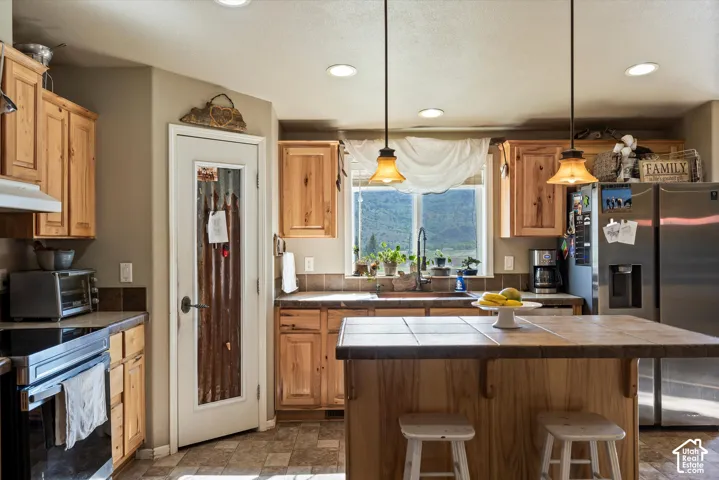 Wood-finish cabinetry, tile countertops, and a stainless steel refrigerator
