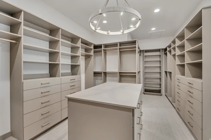 Expansive walk-in closet featuring extensive built-in shelving, multiple hanging rods, generous drawer storage, a central island, and recessed lighting