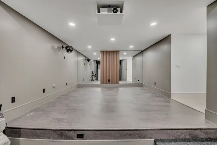 Recessed ceiling lighting, built-in projector, full-wall mirrors, wood-finish accent paneling, and concrete flooring