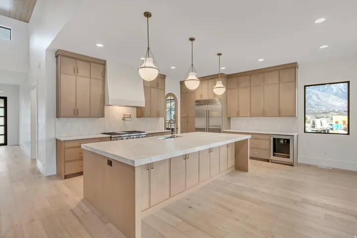 Expansive kitchen featuring wood-finish flooring, light wood cabinetry, a large kitchen island with a light-toned countertop, and stainless-steel appliances