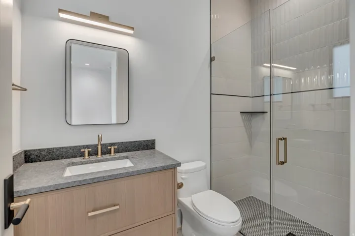 Vanity with stone countertop and integrated sink, framed mirror, and modern light fixture
