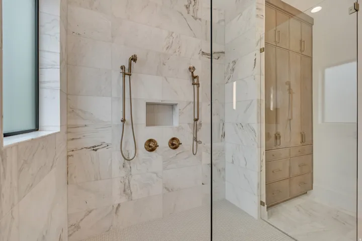 Walk-in shower with marble-look tile walls, dual shower heads, integrated shelf niche, and glass enclosure