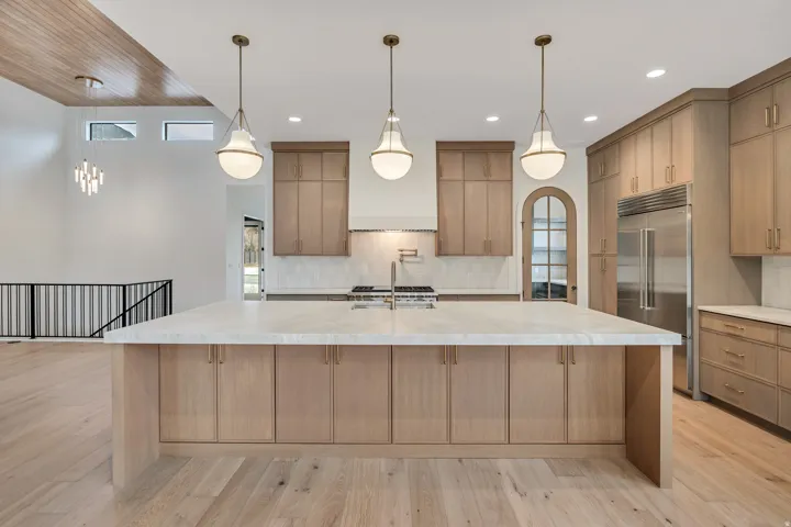 Spacious kitchen island with a light-toned countertop, integrated cabinetry, light wood-finish flooring, and high ceilings with wood-panel accents