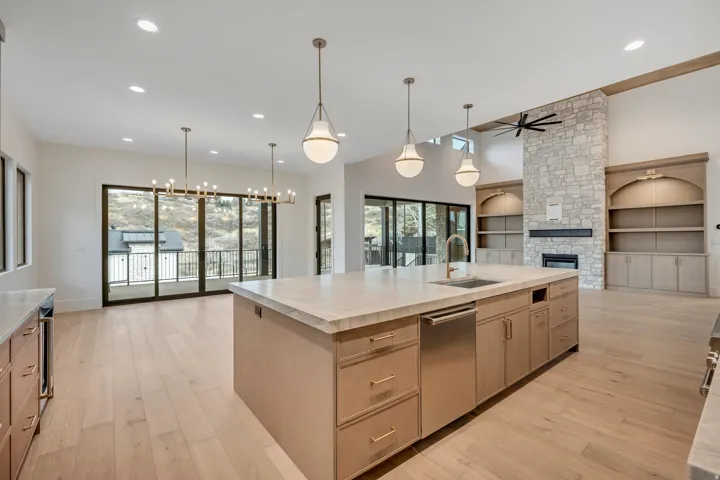 Spacious open-concept living area featuring wood-finish flooring, a stone-clad fireplace, built-in shelving, and a large kitchen island with integrated sink