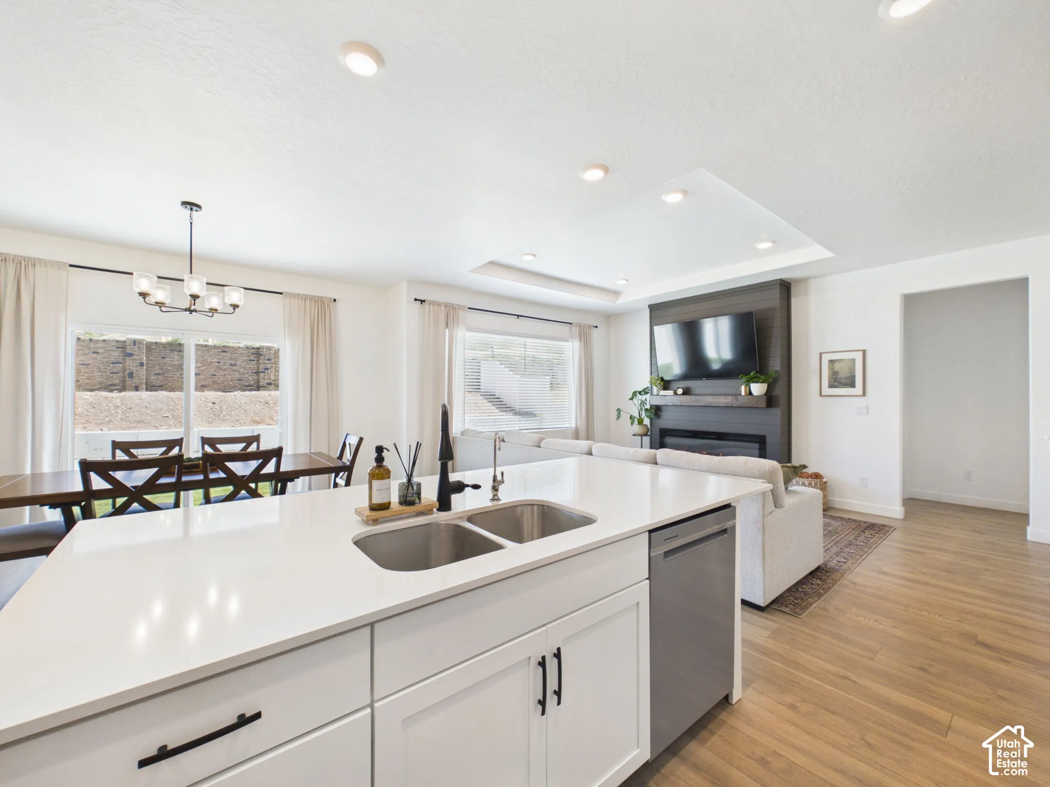 Open-concept living space featuring a kitchen island with dual sinks, recessed lighting, wood-finish flooring, a contemporary fireplace, and large windows