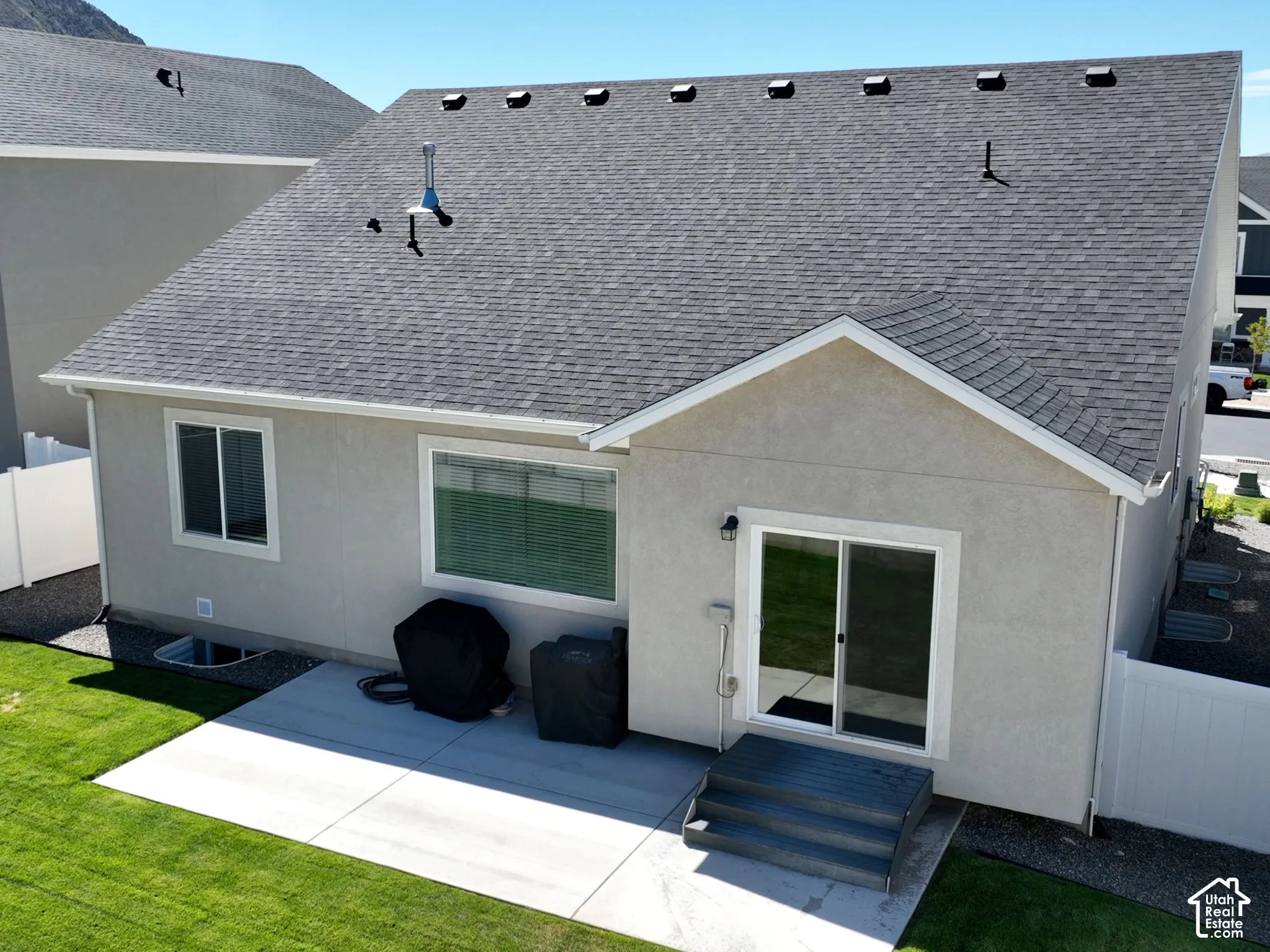 Exterior featuring stucco siding, a grey asphalt shingle roof, a concrete patio, a sliding glass door, and a white privacy fence