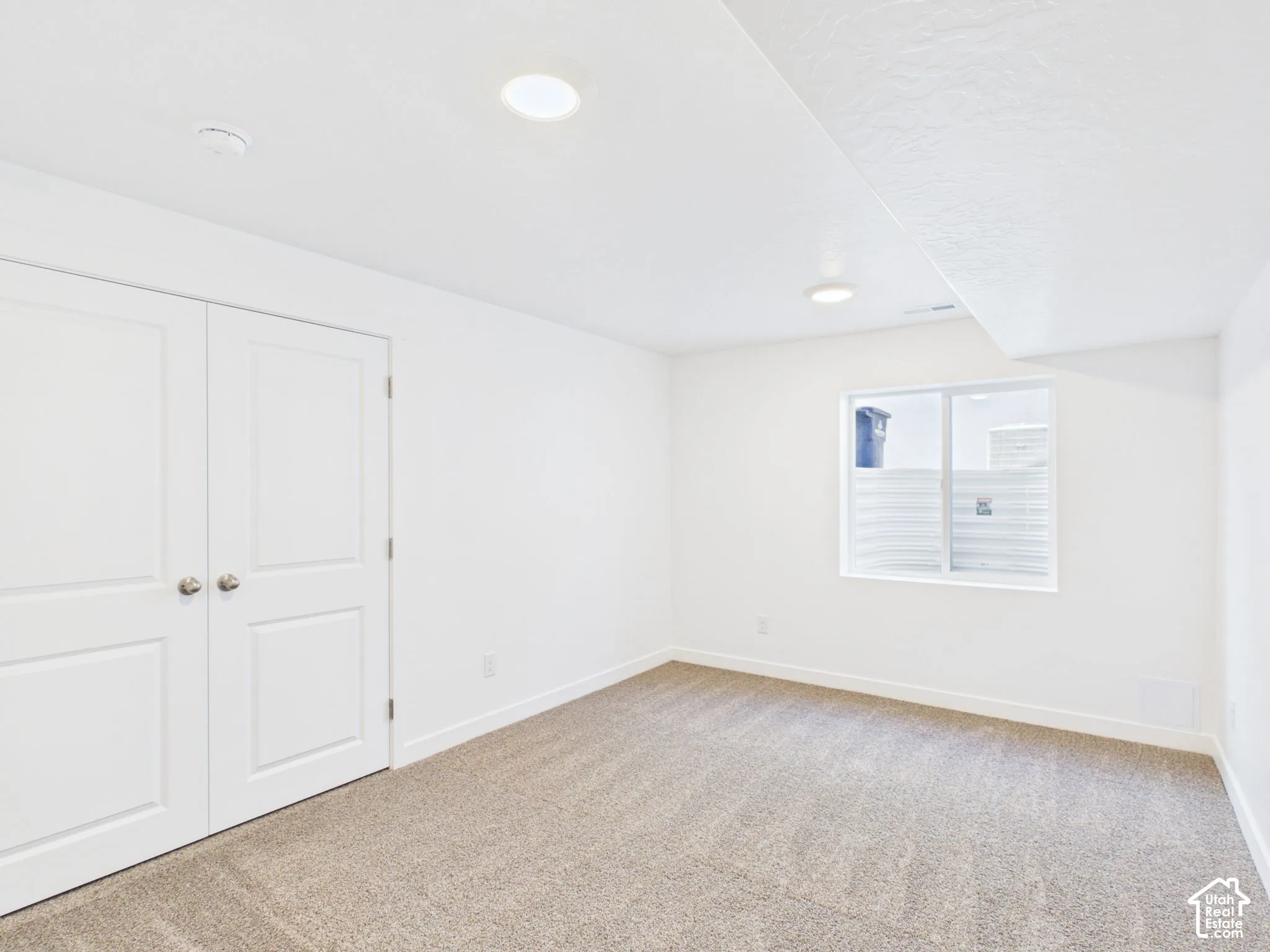 Recessed ceiling lighting, white walls, light-colored carpet, white trim, and a window with privacy film