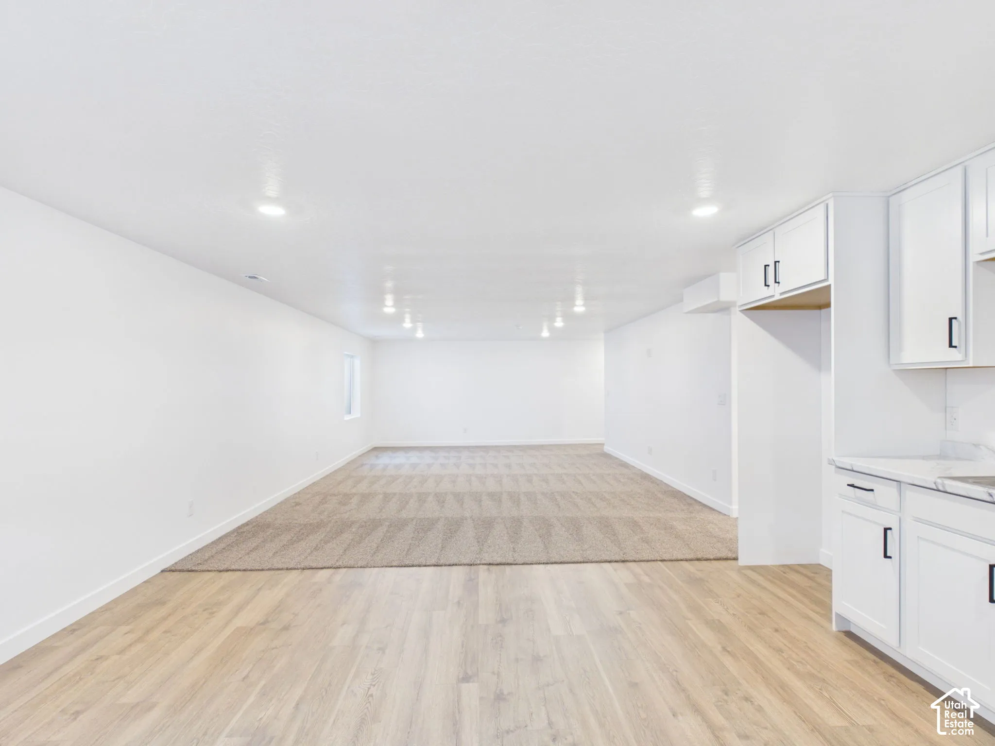 Recessed lighting illuminates the open-concept space featuring wood-finish flooring and a carpeted area