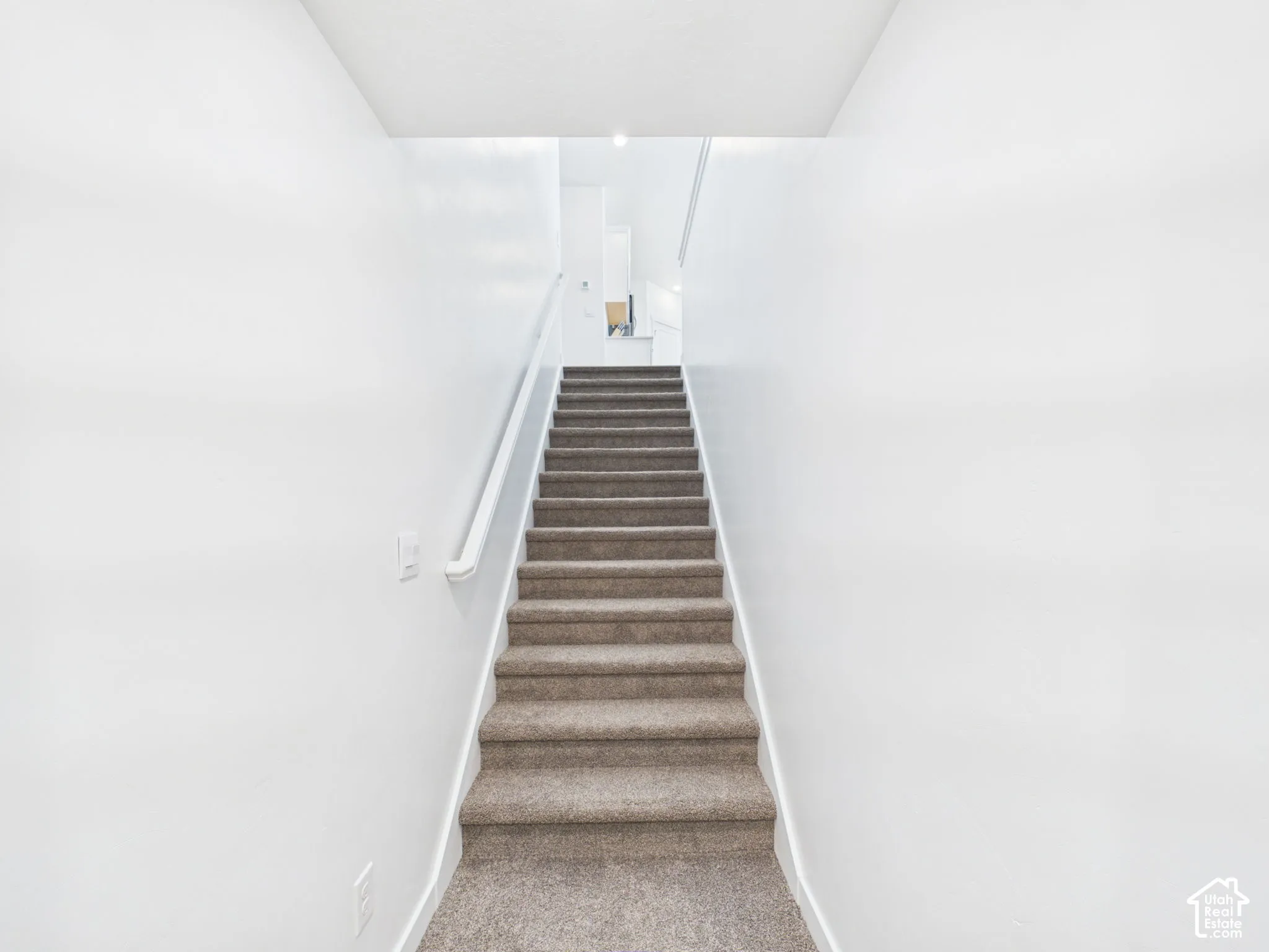 Carpeted staircase with a single handrail and light-toned walls