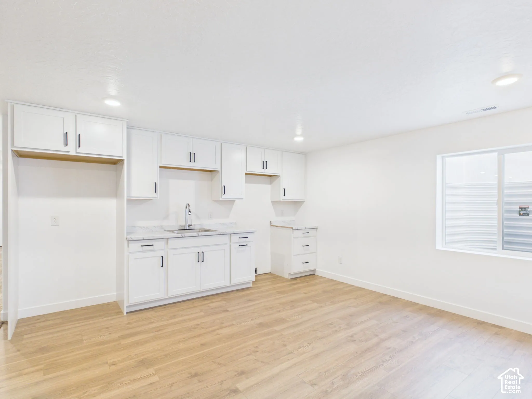 White cabinetry with dark hardware, stone-finish countertops, stainless steel sink with a gooseneck faucet, light wood-finish flooring, and recessed ceiling lighting