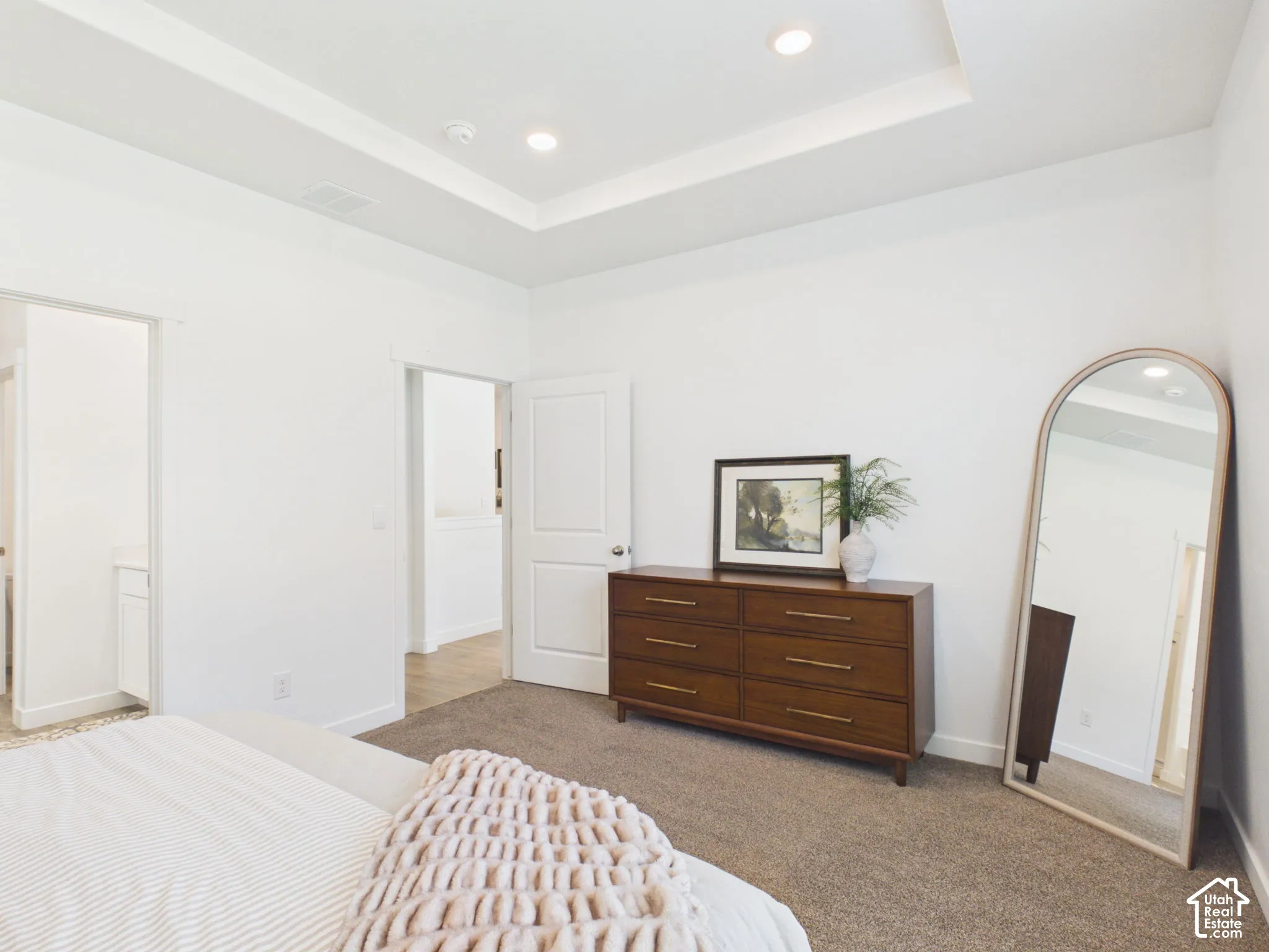 Spacious primary bedroom featuring a coffered ceiling with recessed lighting, light-toned carpet flooring, and abundant natural light