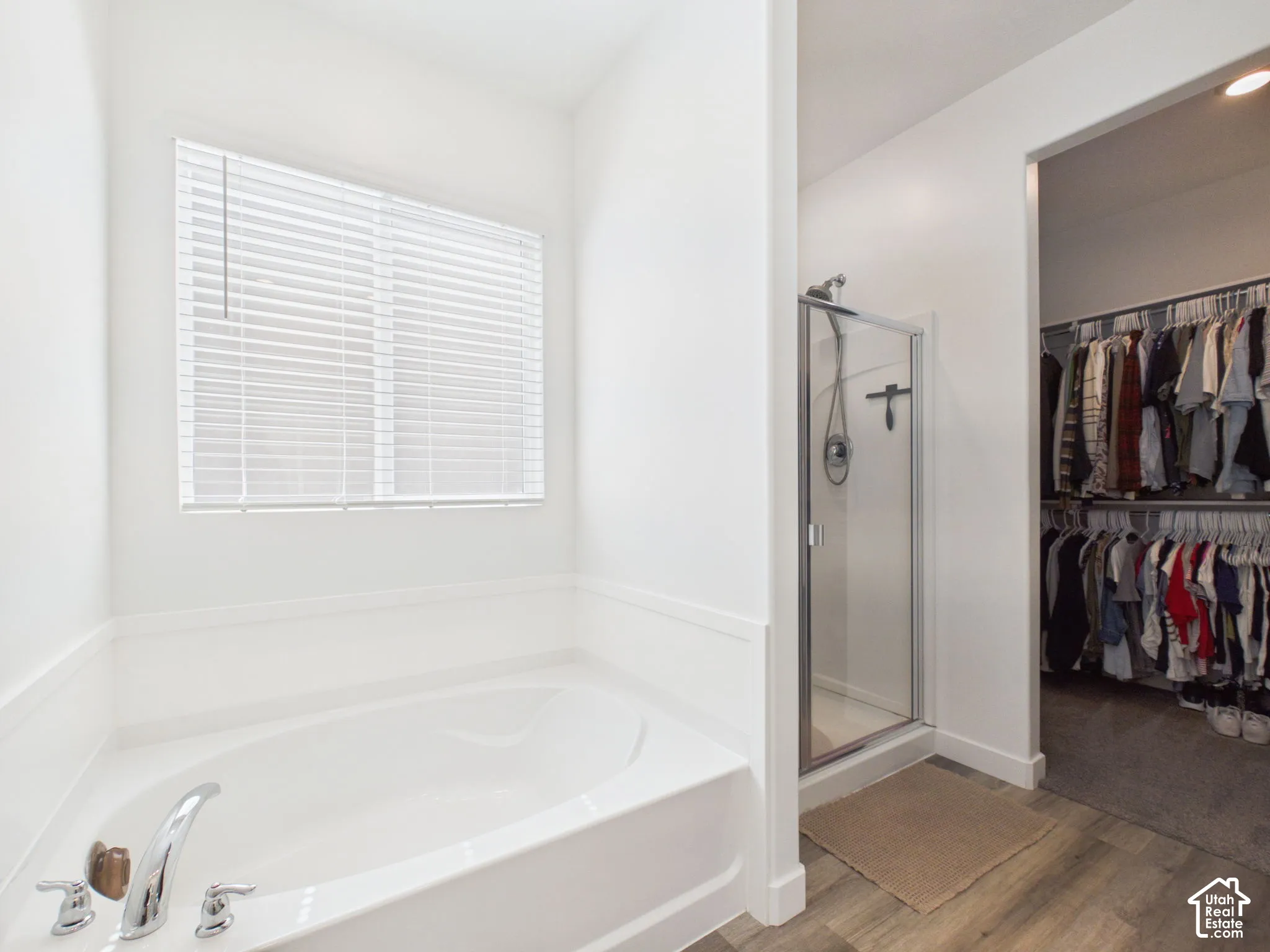 Soaking tub with chrome fixtures, glass-enclosed shower, wood-finish flooring, and a walk-in closet with built-in shelving