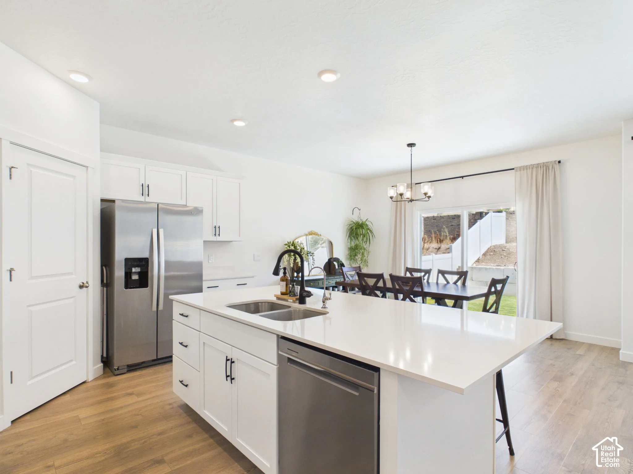 Kitchen featuring a center island with double sink, stainless steel appliances, white cabinetry, and wood-finish flooring