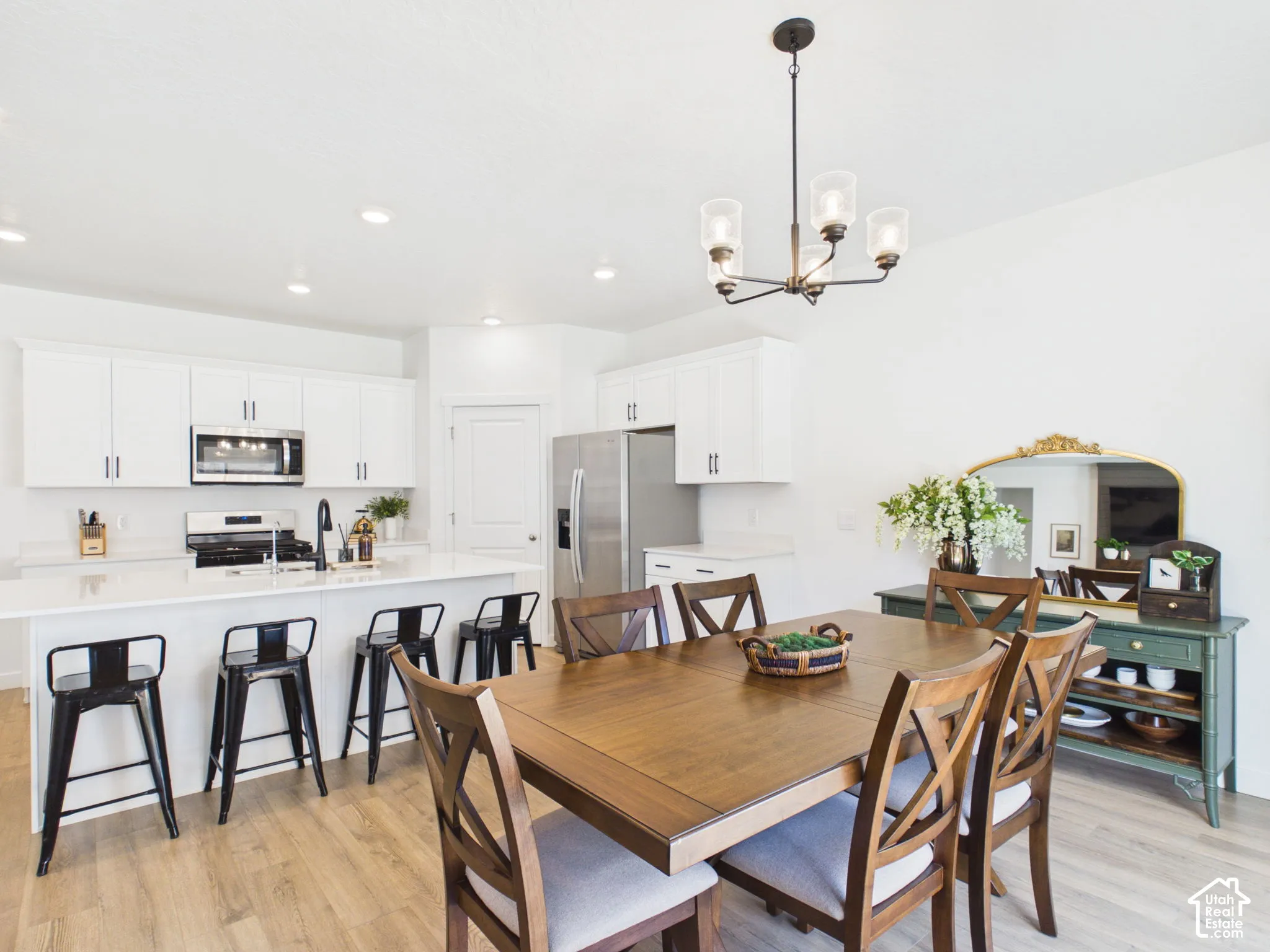 Open-concept kitchen and dining area featuring a kitchen island with seating, stainless steel appliances, white cabinetry, and wood-finish flooring