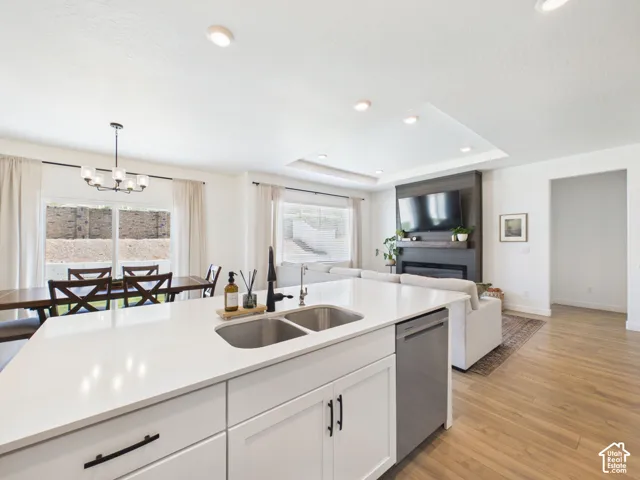 Open-concept living space featuring a kitchen island with dual sinks, recessed lighting, wood-finish flooring, a contemporary fireplace, and large windows