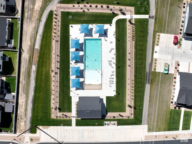 Rectangular swimming pool with integrated tanning ledge, multiple shade structures, surrounding concrete deck, adjacent clubhouse building, and manicured lawn