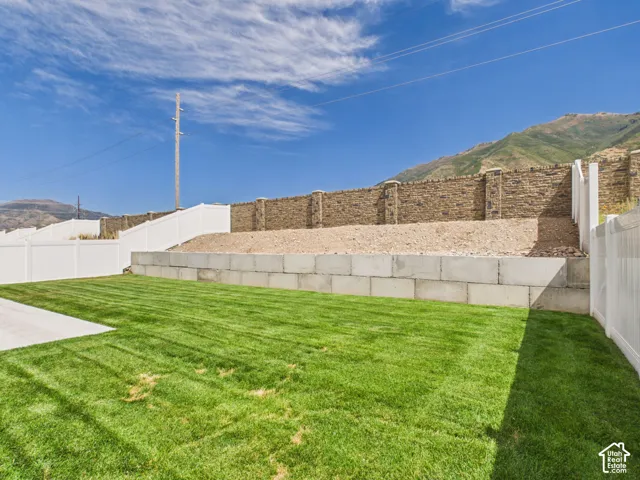 Expansive lawn area with concrete hardscaping, bordered by a white vinyl fence and a stone retaining wall