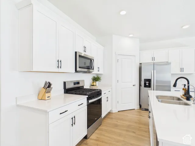 White shaker cabinetry with black hardware, stainless steel appliances, light-toned wood-finish flooring, recessed lighting, and white countertops
