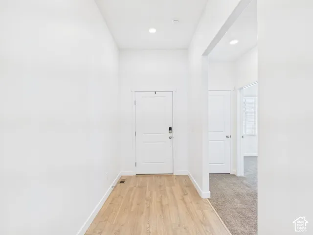 Recessed lighting illuminates the entry, featuring wood-finish flooring transitioning to carpet