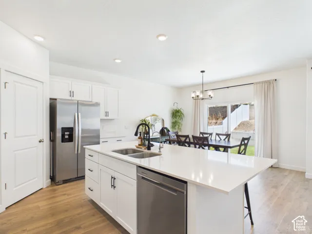 Kitchen featuring a center island with double sink, stainless steel appliances, white cabinetry, and wood-finish flooring