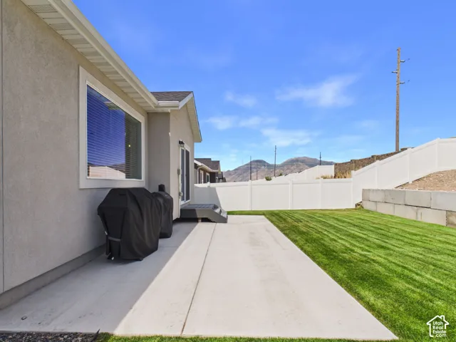 Expansive concrete patio with a manicured lawn, complemented by a white privacy fence and a retaining wall