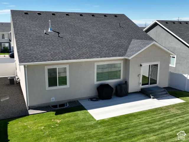 Expansive green lawn with a large concrete patio, sliding glass door access, and a durable asphalt shingle roof