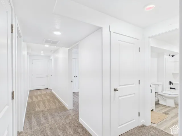 Hallway featuring recessed lighting, a neutral carpet, white panel doors, and a bathroom with a white toilet and black fixtures