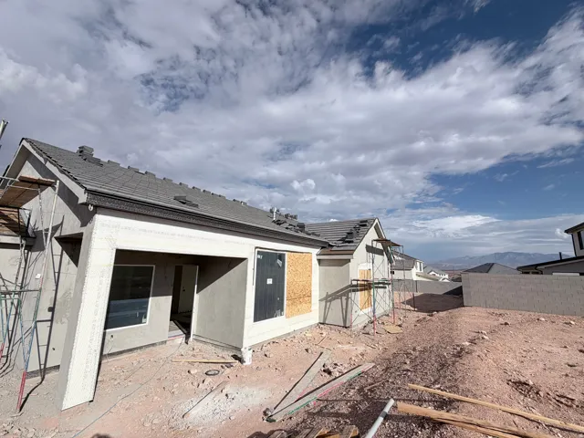 Neutral stucco exterior with a covered patio, dark gray roof tiles, and an unfinished backyard