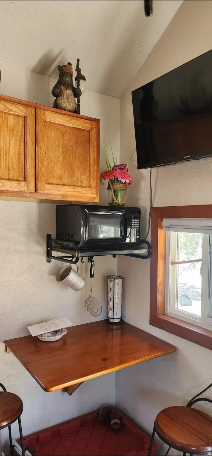 Wood-finish cabinetry, corner-mounted wood-finish tabletop, corner window, wall-mounted television, and wall-mounted microwave shelf