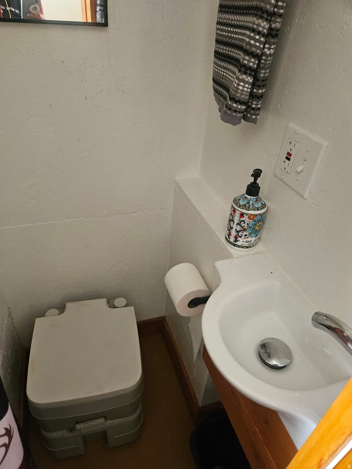 Compact sink with a chrome faucet, wood-finish vanity, and a wall-mounted toilet paper holder