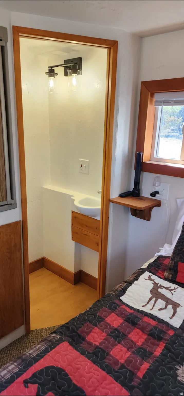 Recessed sink with built-in wood cabinetry, overhead two-bulb vanity light, wood-finish flooring, and natural wood window trim
