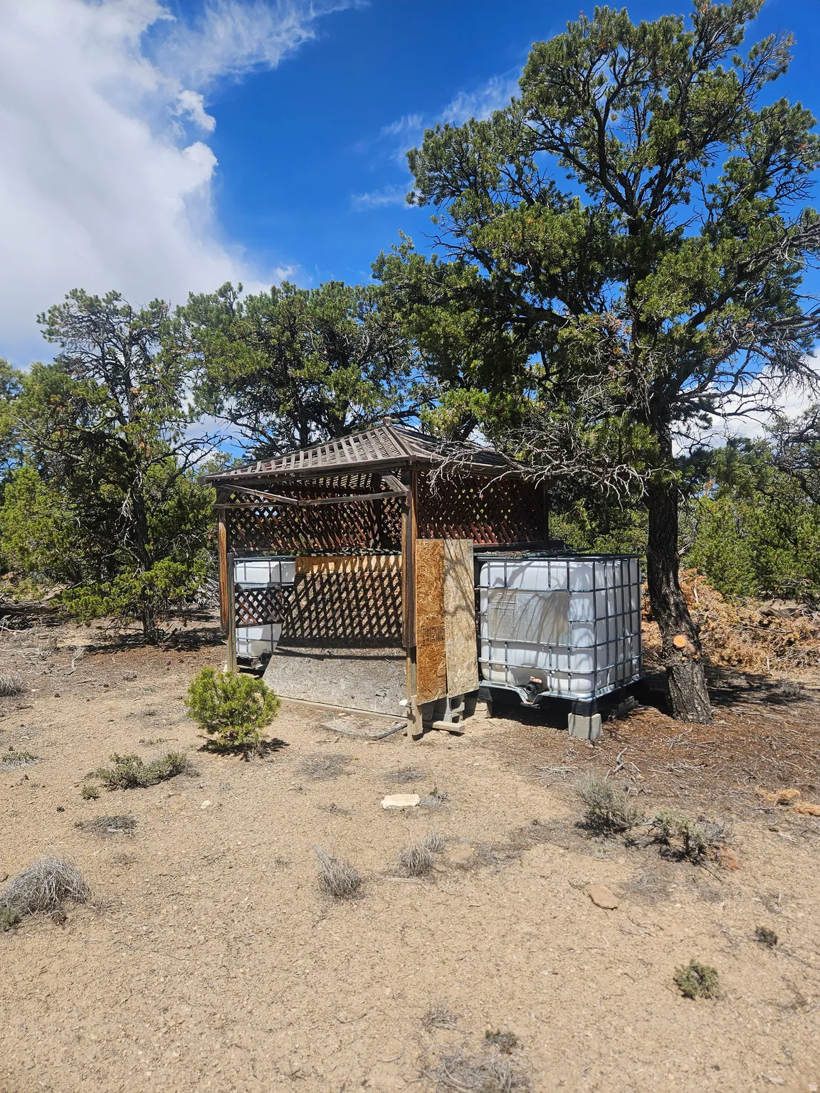 Gabled gazebo structure with lattice walls and a surrounding natural landscape
