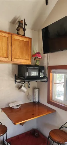 Wood-finish cabinetry, corner-mounted wood-finish tabletop, corner window, wall-mounted television, and wall-mounted microwave shelf