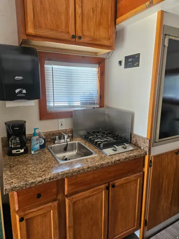 Compact kitchen featuring wood cabinetry, a stainless steel sink, a multi-burner gas cooktop, and speckled countertops