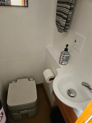 Compact sink with a chrome faucet, wood-finish vanity, and a wall-mounted toilet paper holder
