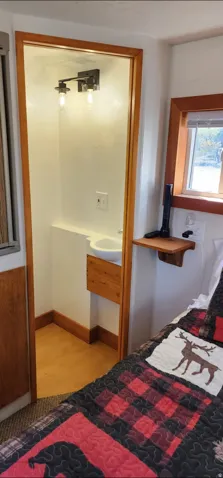 Recessed sink with built-in wood cabinetry, overhead two-bulb vanity light, wood-finish flooring, and natural wood window trim