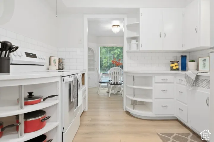 White cabinetry, subway tile backsplash, light wood-finish flooring, built-in open shelving, and integrated electric range