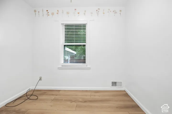 White walls, wood-finish flooring, and natural light from a window with blinds
