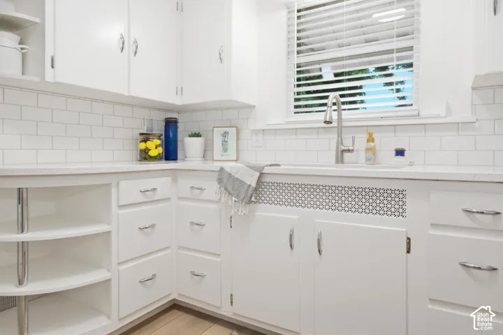 White cabinetry, subway tile backsplash, white countertops, stainless steel kitchen faucet, and wood-finish flooring
